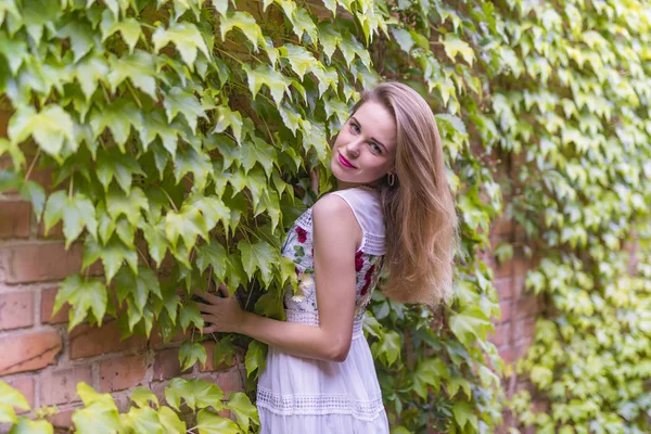 Chica en el fondo de una pared con follaje verde — Foto de Stock