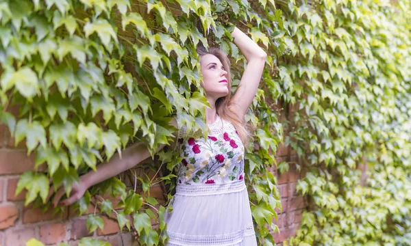 Flicka på bakgrunden av en vägg med grönt bladverk — Stockfoto