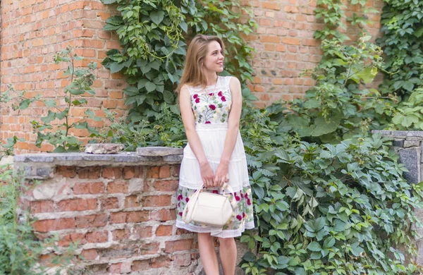 Fille avec sac à main près d'un mur avec des feuilles vertes — Photo