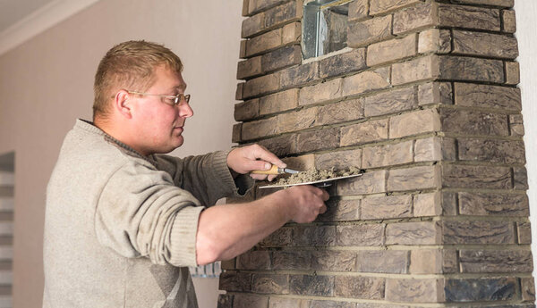 Процесс трения шва между плитками на камине в комнате
