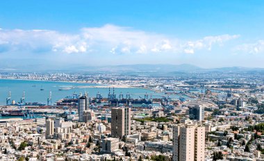 Limanı olan bir şehir, arka planda deniz ve bulutlarda dağlar olan bir sürü ev.