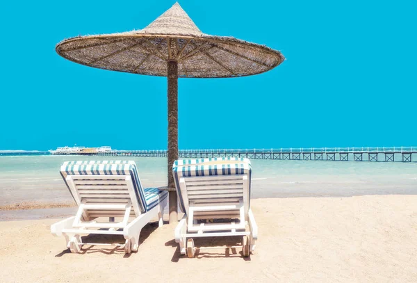 Σαλόνι μονίππων και ομπρέλες στην παραλία κατά το γαλάζιο του ουρανού και — Φωτογραφία Αρχείου
