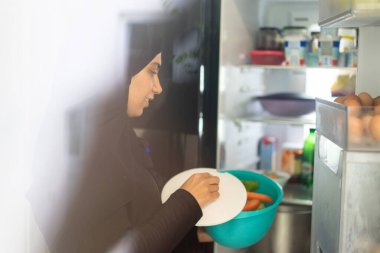 Müslüman peçeli kadın mutfakta buzdolabı kullanıyor.