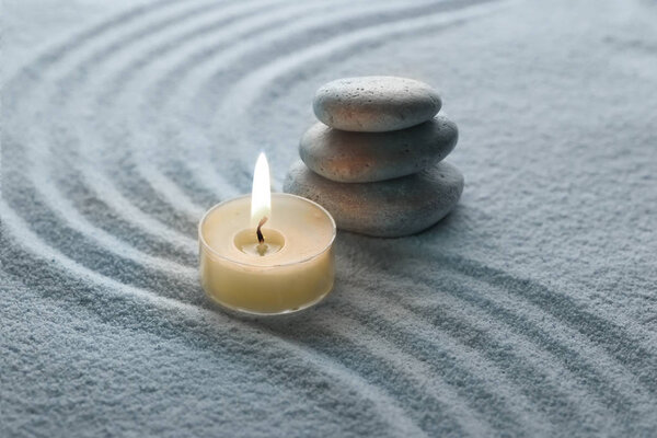 light warm candle and stone on sand 
