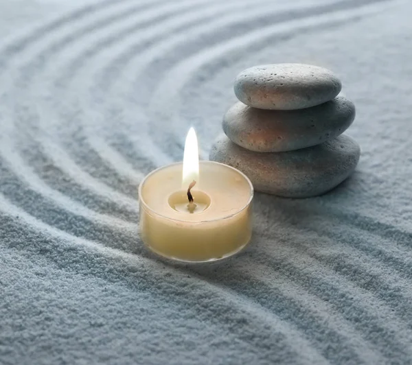 Lehká teplá svíčka a kámen v písku — Stock fotografie