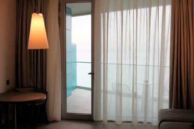 Balkona açılan cam kapılı oturma odası. Deniz manzaralı.