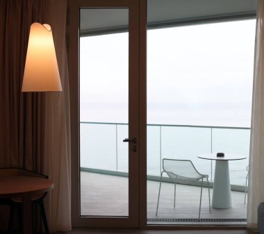 Balkona açılan cam kapılı oturma odası. Deniz manzaralı.