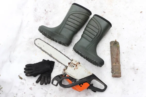 Chainsaw, pare of gloves, two boots and log on the snowy backgro — Stock Photo, Image