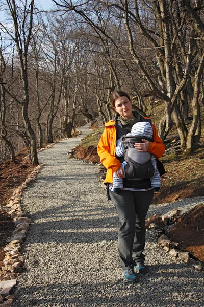 Mamma med barn i bärsele promenader genom skogen grusvägen — Stockfoto