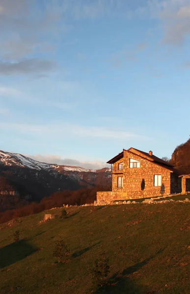 Rumah batu kesepian di bukit di latar belakang pegunungan bersalju, saat matahari terbit, vertikal — Stok Foto