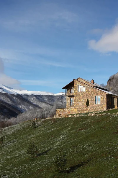 Solitaria casa de piedra en la colina en el fondo de las montañas nevadas, nubes — Foto de Stock