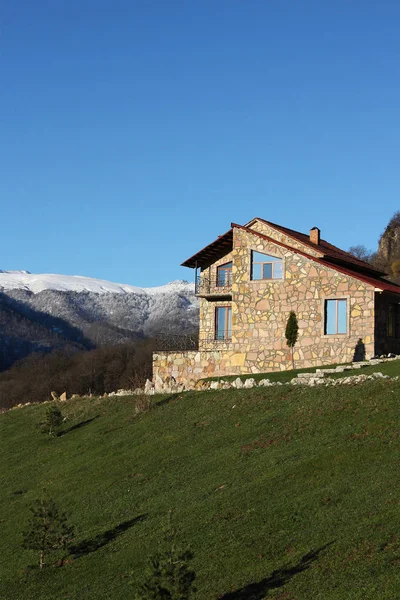 Solitaria casa de piedra en la colina en el fondo de las montañas nevadas, cielo azul claro, vertical — Foto de Stock