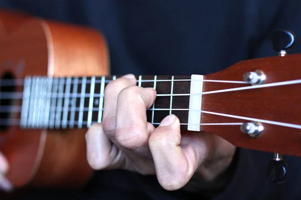 Left musician hand clamps the chord on the ukulele fretboard — Stock Photo, Image