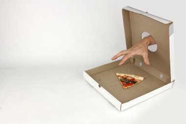 İnsan eliyle fast food kutusundaki delikten son dilim pizzayı, beyaz arka planı, açgözlülük kavramını almaya çalışır.