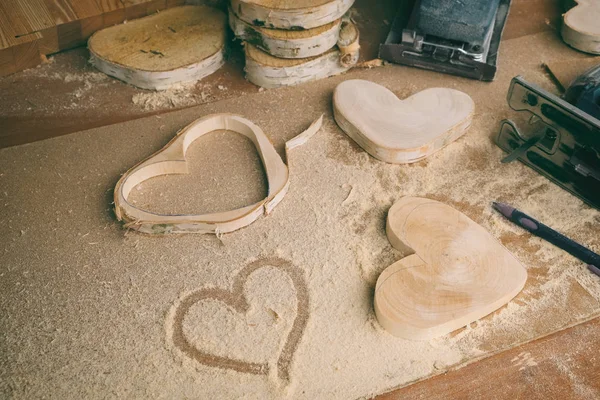 Menuisier lieu de travail gros plan, ébauches en bois en forme de coeur, sciure de bois et outils de menuiserie, cadeau de Saint-Valentin fait à la main — Photo
