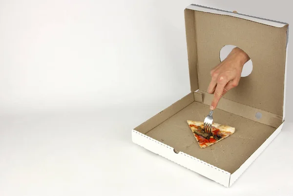 Kéz a lyukon keresztül gyorskaja karton doboz impales a villán az utolsó szelet vegetáriánus pizza, koncepció kapzsiság — Stock Fotó