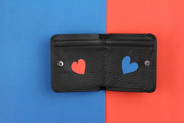 Чорний шкіряний гаманець з двома ремісничими паперовими сердечками червоного та синього кольорів на фоні кольорових паперів, концепт-валентний подарунок або хороші інвестиції — стокове фото
