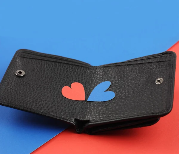 Black leather wallet with two craft paper hearts red and blue on color papers background, side view, concept valentine gift or real wealth — Stock Photo, Image