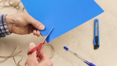 Adam kırmızı makasla smal mavi kağıt kalp kesiyor, Sevgililer Günü için el işi hediyesi, atölye masaüstü görüntüsü  