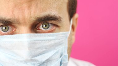 Pembe arka planda tıbbi maskeli yakın plan, ciddi araştırma bilim adamı doktor dikkatle ve dikkatlice, virüse veya koronavirüse karşı araştırma veya geliştirme aşısına bakıyor 