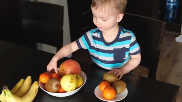 小孩选择新鲜水果作为素食早餐 拿苹果 放在盘子里 素食小孩坐在厨房的桌子上 男孩吃富含维生素的健康食品作为免疫力 — 图库视频影像