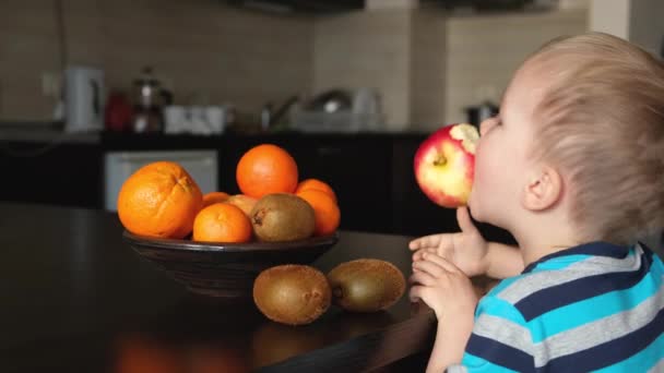 小さなかわいいビーガンの子供は彼の口の中でリンゴを保持し 周りを欺く キッチンで楽しいを持っています ビーガンまたはベジタリアン健康的な食品朝食 新鮮な果物とプレート サイドビュー — ストック動画