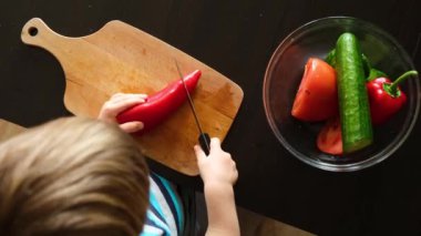 Küçük vejetaryen çocuk dikkatle keser ve kırmızı biberi bıçakla görür, vejetaryen çocuk mutfakta sebze salatası pişirir, montessori eğitim becerisi, üst manzara