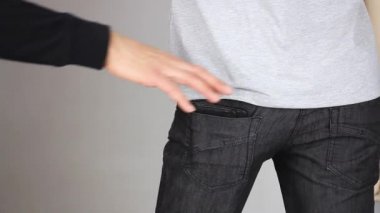 Hırsız gizlice kurbanın pantolonunun arka cebinden deri cüzdanı, yankesicilik suçu, gri arka plan, yakın plan. 