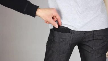 Yankesici, siyah pantolonlu birinin arka cebinden nazikçe deri cüzdan çıkarır. İki parmak, yankesicilik suçu, yakın plan.