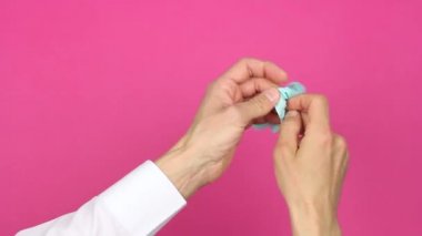 İnsan eli, sağ eline mavi tıp eldiveni, birinci şahıs görünümü, pembe arka plan, hijyen ve virüs salgını veya kirliliğinin önlenmesi kavramını takar