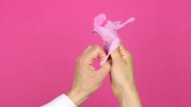 İnsan eli, sağ eline pembe tıbbi eldiven, birinci şahıs görüşü, pembe arka plan, hijyen konsepti ve virüs salgını veya kirliliği önleme konsepti takıyor.