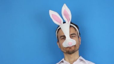 Paskalya tavşanı maskeli ve eldivenli bir adam gülümseyerek tıbbi maske takıyor, tatillerde karantina, virüs veya kirlilik koruması ve önleme, parti hazırlığı, mavi arkaplan kopya alanı