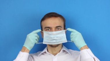 Merkezdeki erkek yüzüne önden bakmak, tıbbi maske takmanın, virüs koronavirüsünün önlenmesinin veya korunmasının veya kirliliğin, mavi arka planın nasıl gösterildiğini göstermek 