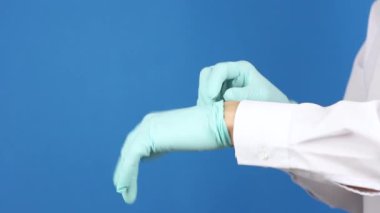 İnsan elleri mavi ameliyat eldivenlerini çıkarıp çöpe atar, yan görüş, mavi arka plan, virüsün sonu veya koronavirüs salgını kavramı ya da kirlilik karantinasını bitirir.