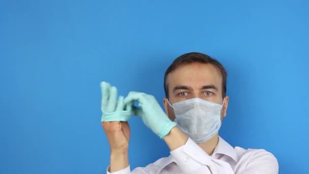 フロントビュー医療用マスクを持つ男性の顔 医療用手袋を着用し ウイルスのコロナウイルスや汚染の予防または保護 医師または患者は タイトルのコピースペースと青の背景を実証 — ストック動画
