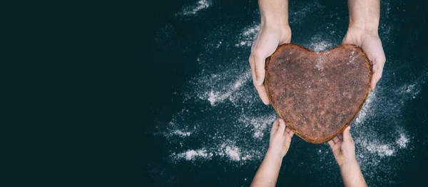 father baker hands gives vegan rye whole grain yeast-free sourdough bread in shape heart to son kid, sustainable living, concept pass of experience and knowledge, continuity of generations, copy space