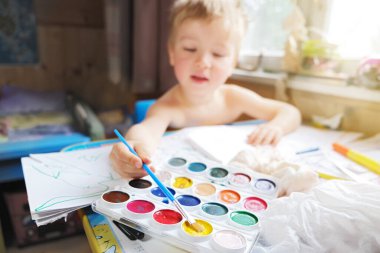 Küçük çocuk çocuk masasına oturur ve suluboya ve boya fırçasıyla resim çizer, karantina karantinasında evde eğitim, montessori eğitimi...