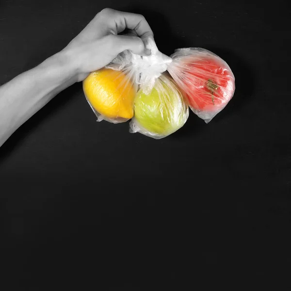 手拿着水果 西红柿和柠檬 各装一个塑料袋 隔离中的环境污染问题 安全分娩的概念 带有复制空间的黑色背景 — 图库照片