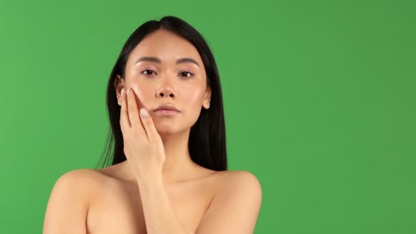 Une belle fille d'apparence asiatique aux épaules nues avec une expression faciale argentée regarde la caméra, le concept de la beauté d'un corps sain et d'une belle peau — Video