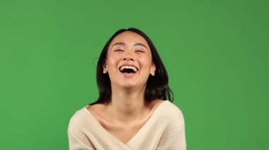 Güzel, neşeli, komik, Asyalı bir kız yüzünde az miktarda makyajla kamera karşısında mutlu bir şekilde gülümsüyor. Olumlu bir ruh hali, neşe ve eğlence anlayışı.