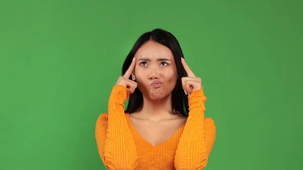 Asiatin hält ihren Zeigefinger in der Nähe des Tempels vor der Kamera auf grünem Hintergrund für traurige Gefühle und Sorgen — Stockfoto