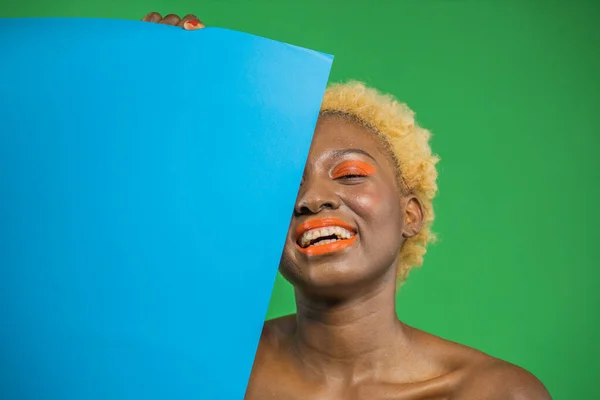Afrikansk amerikansk vacker kvinna täcker blått ansikte halvt leende visar vita tänder, isolerad grön bakgrund — Stockfoto