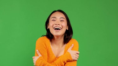 Güzel, neşeli, enerjik, pozitif Asyalı kız izole bir arka planda kendine sarılıyor..