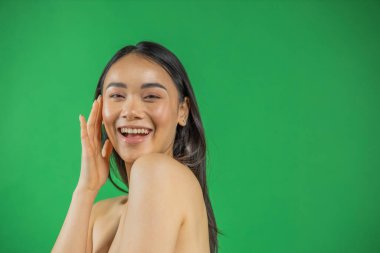 Açık yeşil arka planda fotokopi alanı gösteren mutlu genç Asyalı kadın, mutluluk ve neşe kavramı