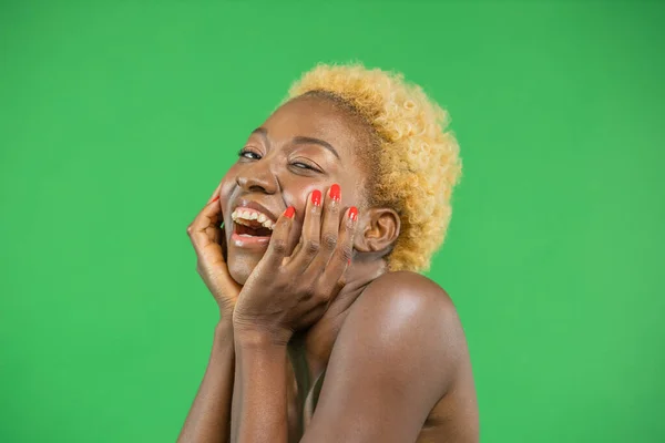Vacker svart kvinna med afro hår har roligt leende och håller hennes ansikte med båda händerna på en isolerad grön bakgrund — Stockfoto