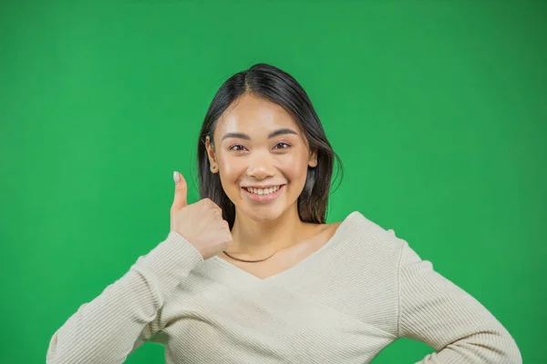 Anatraente jovem mulher asiática mostrando polegares para cima sobre fundo verde — Fotografia de Stock