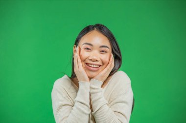 Yeşil arka planda gülümseyen, şaşkın, heyecanlı bir kadın. Neşeli, çok yönlü bir Asyalı, Çinli kadın model neşelidir.