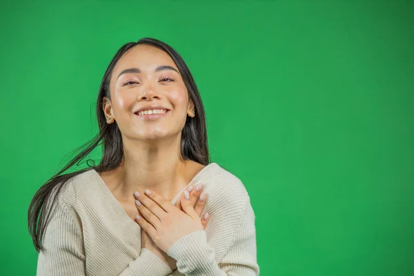 Привлекательная, очаровательная и женственная азиатка с крупным планом, прижимает руки к груди, широко хихикает и улыбается, весело смотрит в камеру, проявляя позитивность и оптимизм — стоковое фото