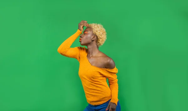 Femme afro-américaine avec coupe de cheveux courte en chemisier orange vif tenant sa main sur sa tête se tient sur fond vert isolé, concept de vacances — Photo
