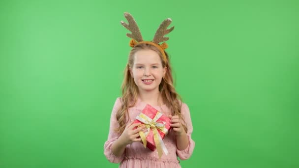 Bonne petite fille souriante avec boîte cadeau rouge. Concept de Noël. Sourire drôle fille en bois de cerf sur fond vert — Video